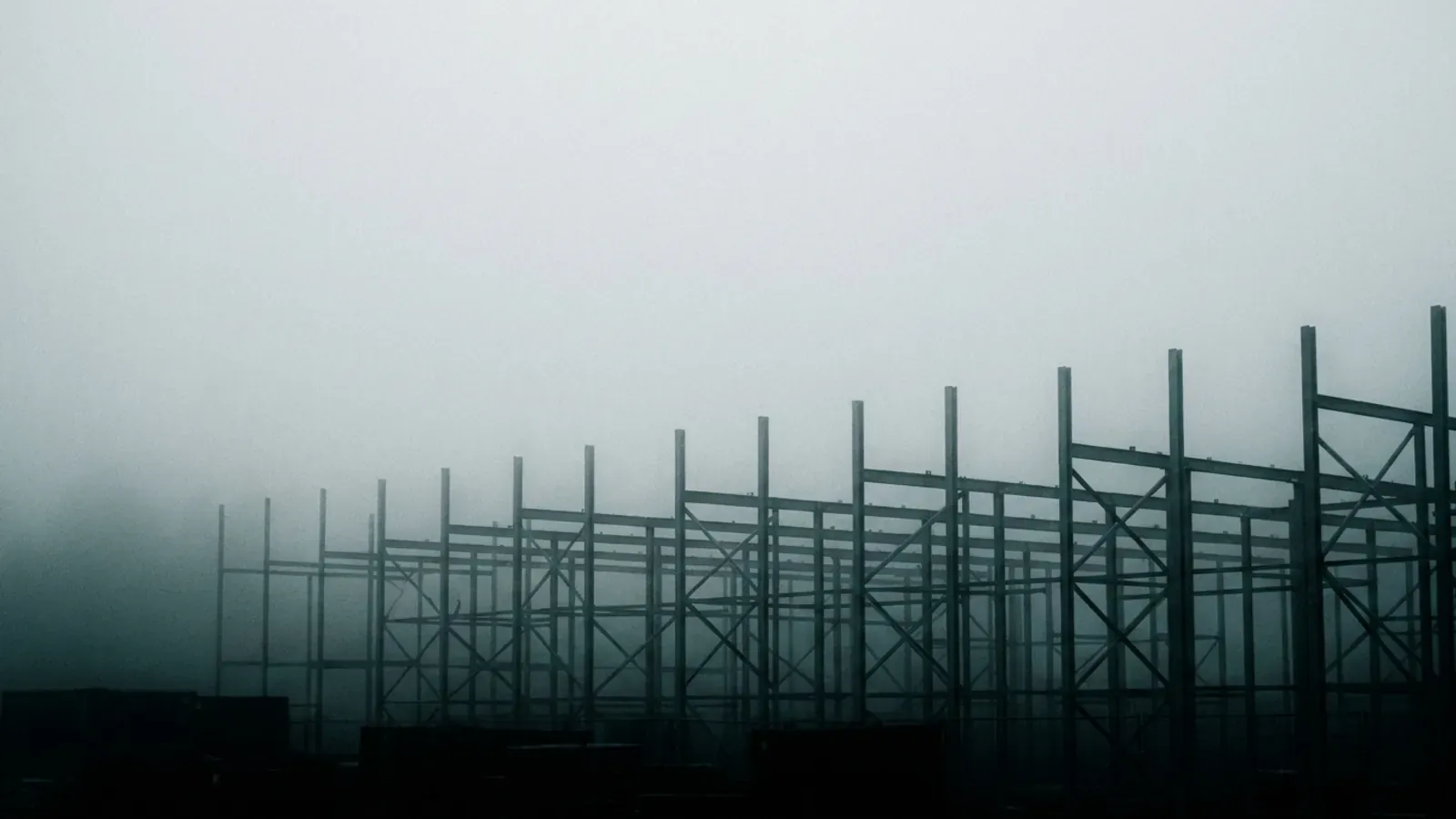 Bare scaffolding standing in fog, the structure around the work rather than the work itself